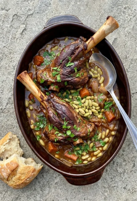 Braised lamb shanks with flageolet beans, carrots and parsley in a dark casserole dish