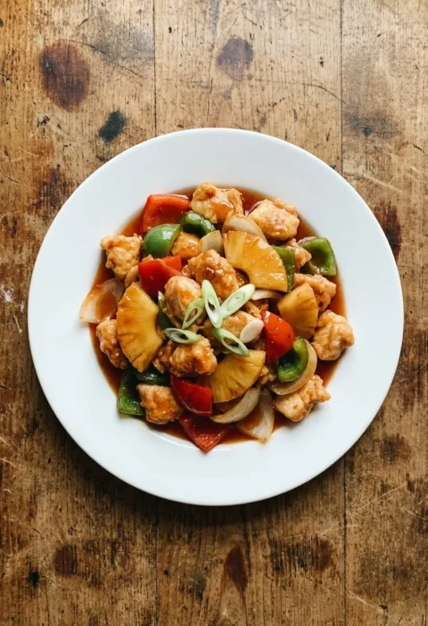 Sweet and sour chicken with peppers and pineapple in a glossy sauce on a white plate