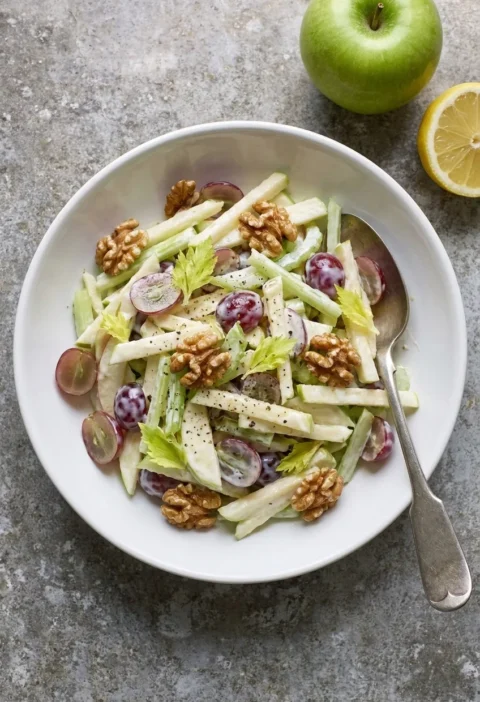 Waldorf salad with sliced apple, celery, red grapes, toasted walnuts and homemade mayo in a white bowl