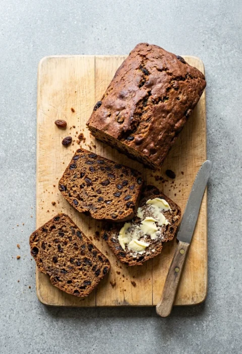 Hairy Bikers bara brith Welsh tea loaf sliced on a wooden board, showing dried fruit through the crumb with one buttered slice