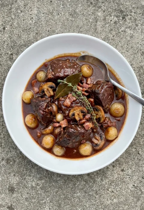 Beef bourguignon in a white bowl with baby onions, mushrooms, and thyme