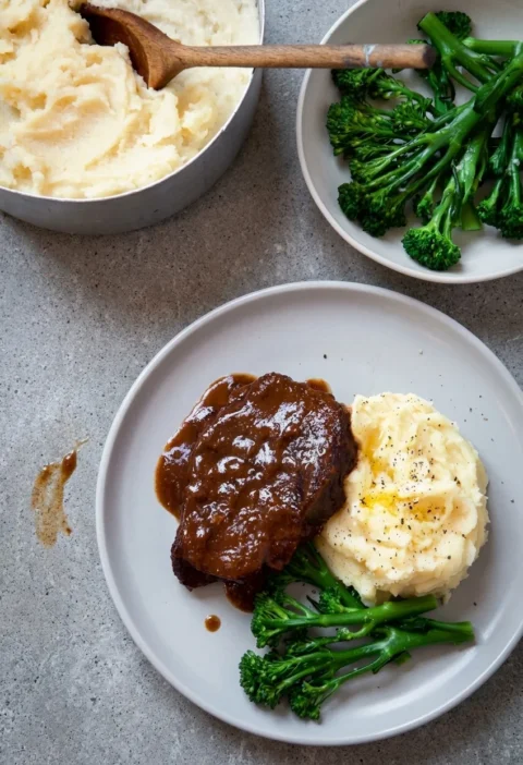 Hairy Bikers braised beef, a glazed piece of feather blade in glossy red wine sauce with buttery mashed potato and tenderstem broccoli on a grey plate