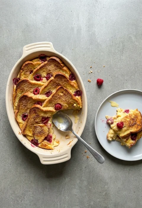 Hairy Bikers bread and butter pudding with golden brioche slices and raspberries in an oval dish, one portion served on a plate