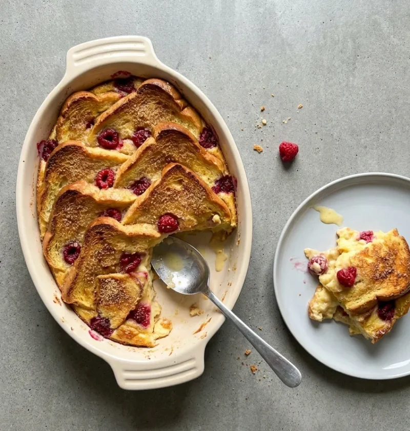 Hairy Bikers bread and butter pudding with golden brioche slices and raspberries in an oval dish, one portion served on a plate