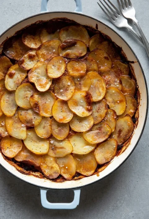 Hairy Bikers corned beef hotpot in a white casserole, overlapping golden crisped potato slices with sea salt and black pepper over layers of corned beef and onion gravy