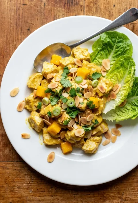 Coronation chicken with diced mango, toasted almonds, coriander, and lettuce on a white plate