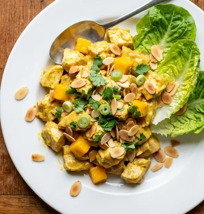 Coronation chicken with diced mango, toasted almonds, coriander, and lettuce on a white plate