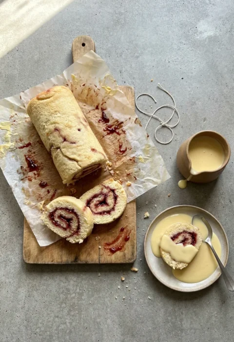 Hairy Bikers jam roly poly unwrapped from its baking paper with thick slices showing raspberry jam spirals and a jug of custard
