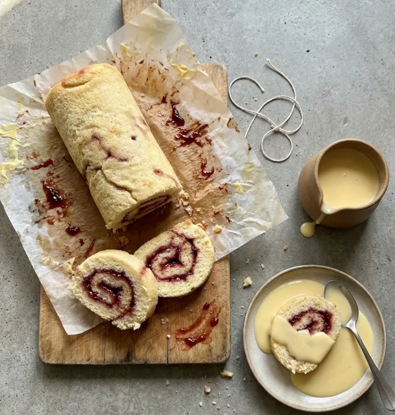 Hairy Bikers jam roly poly unwrapped from its baking paper with thick slices showing raspberry jam spirals and a jug of custard