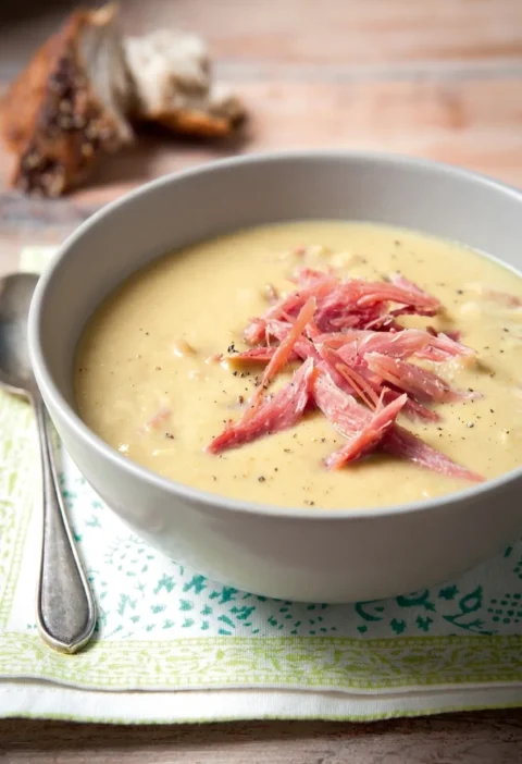 Hairy Bikers pea and ham soup in a grey bowl, topped with shredded ham hock and cracked black pepper
