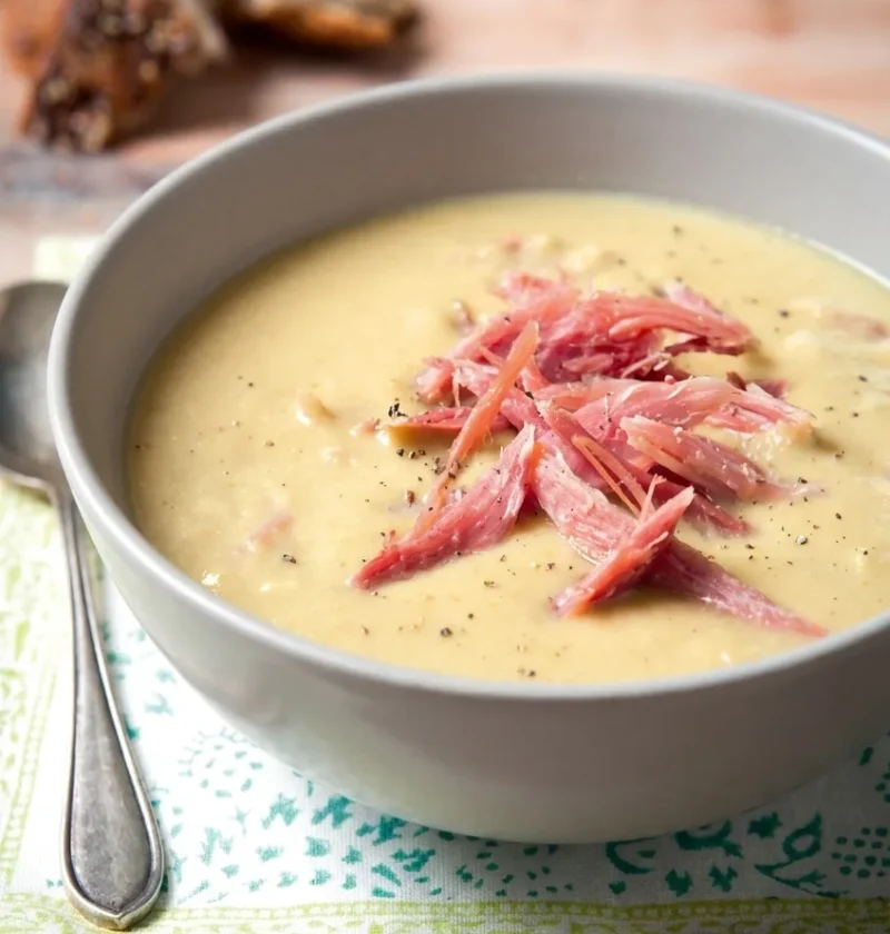 Hairy Bikers pea and ham soup in a grey bowl, topped with shredded ham hock and cracked black pepper
