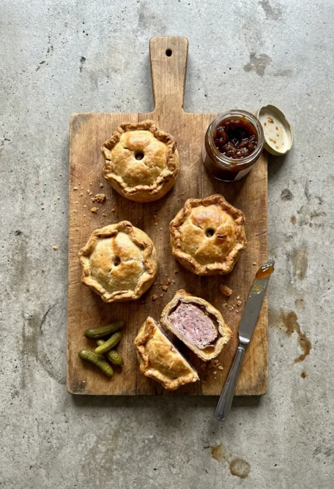 Hairy Bikers pork pie batch of four hand raised pies with one cut open showing the pork filling and amber jelly layer