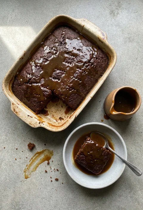 Hairy Bikers sticky toffee pudding in a baking dish with toffee sauce soaked into the dark sponge and one portion served in a bowl