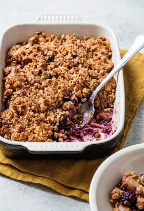 Hairy Bikers apple and blackberry crumble in a cream baking dish with a golden oat topping and purple blackberry juice bubbling underneath