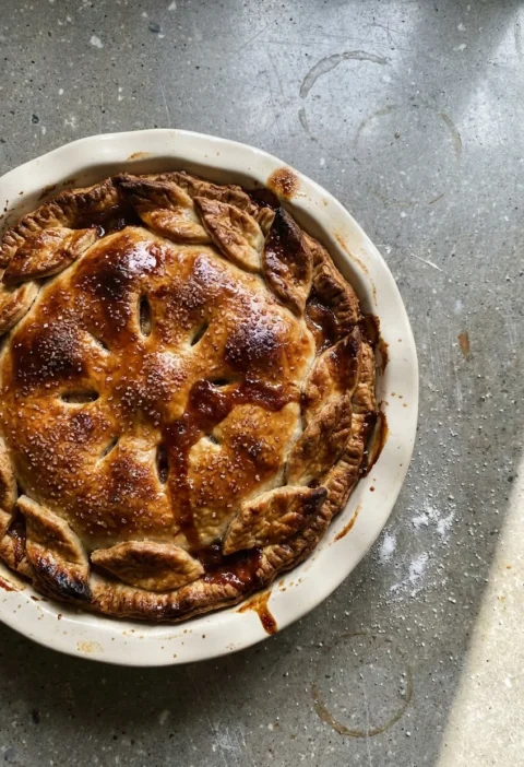 Hairy Bikers apple pie in a ceramic dish with a crimped edge, pastry leaves round the rim and sugar scattered over the golden lid