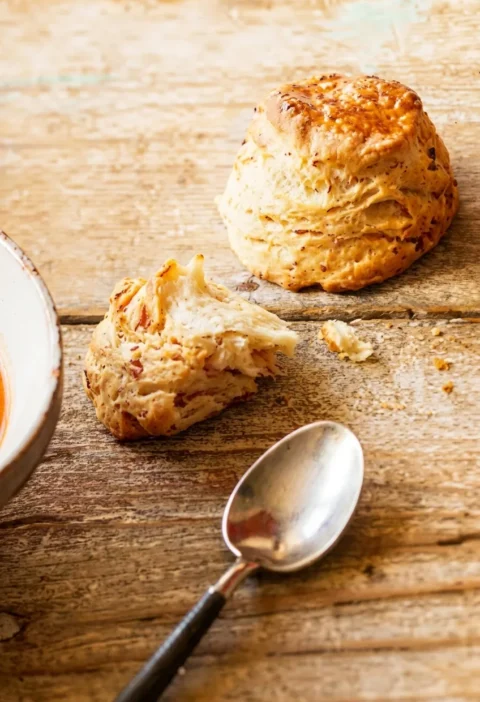 Hairy Bikers bacon scones on a wooden table, golden and glazed, one torn open showing a soft crumb flecked with bacon