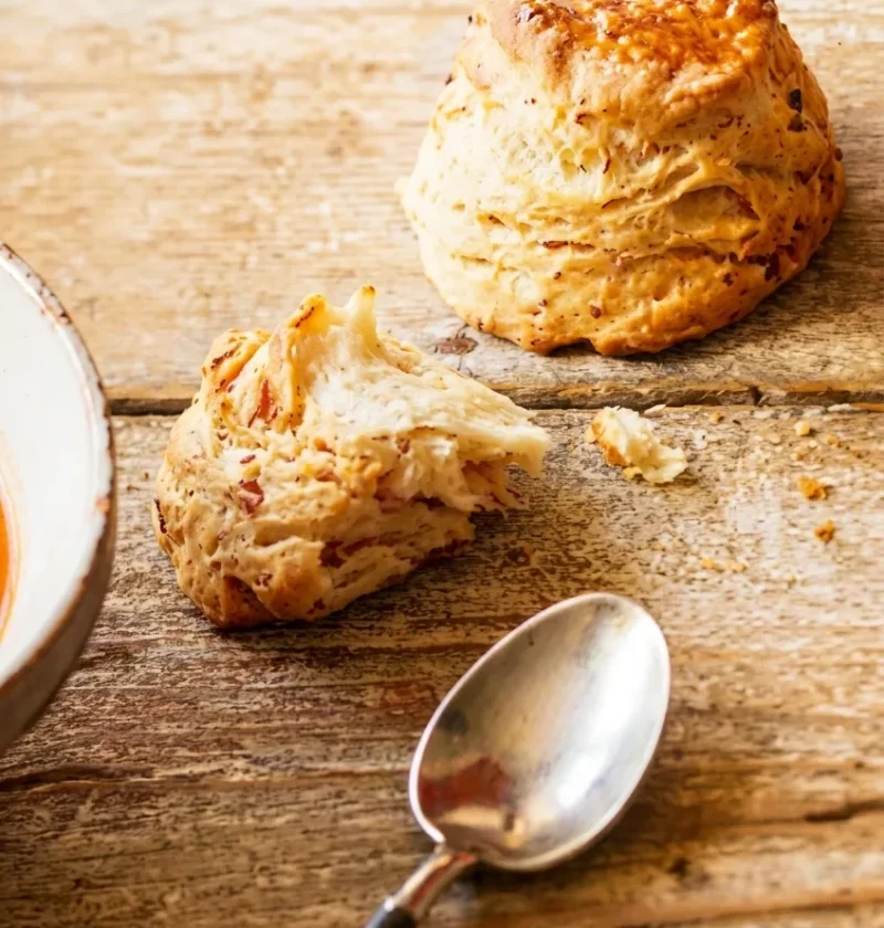 Hairy Bikers bacon scones on a wooden table, golden and glazed, one torn open showing a soft crumb flecked with bacon