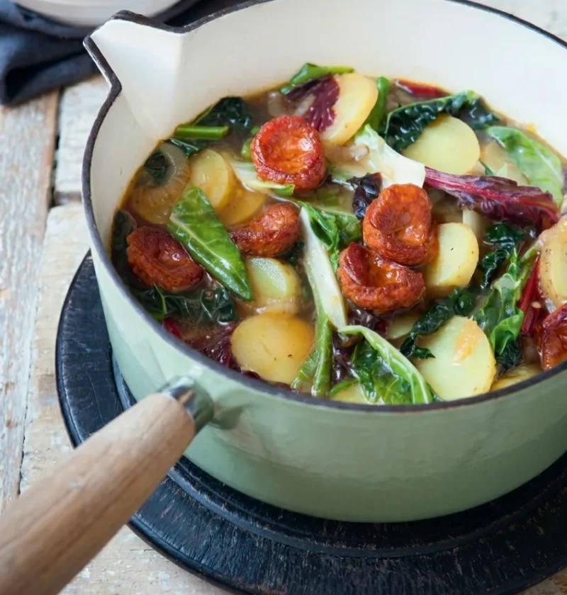 Hairy Bikers caldo verde in a casserole pan with chorizo slices, halved waxy potatoes and shredded greens in a golden broth