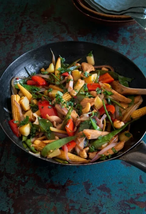 Hairy Bikers chicken stir fry in a black wok with baby corn, mangetout, red pepper, pineapple, cashews and coriander