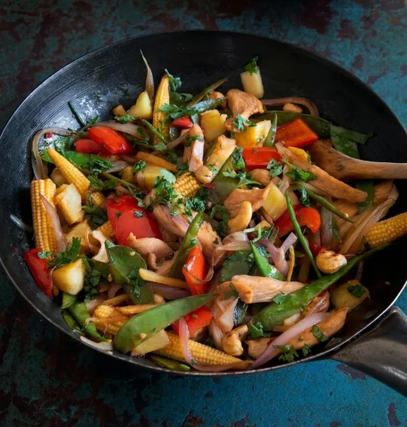 Hairy Bikers chicken stir fry in a black wok with baby corn, mangetout, red pepper, pineapple, cashews and coriander