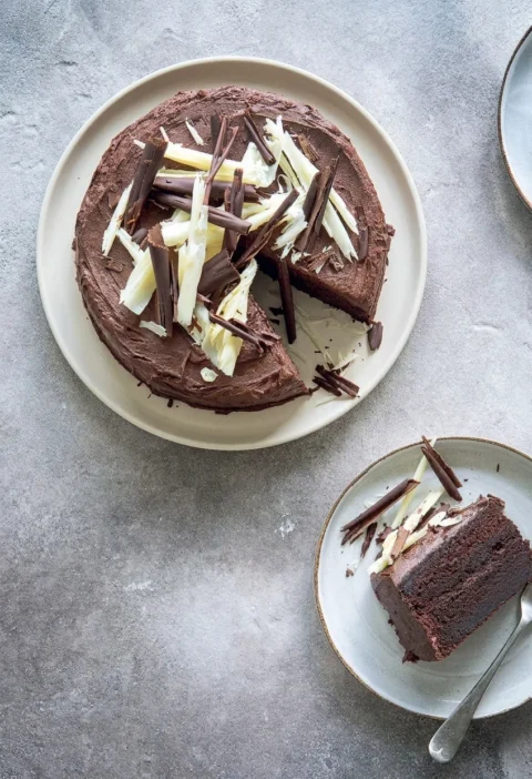 Hairy Bikers chocolate cake covered in chocolate buttercream and topped with dark and white chocolate curls, with one slice cut to show the two sponge layers