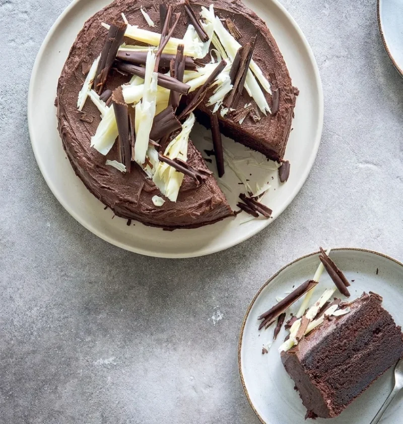 Hairy Bikers chocolate cake covered in chocolate buttercream and topped with dark and white chocolate curls, with one slice cut to show the two sponge layers