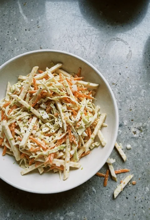 Hairy Bikers coleslaw in a cream bowl with celeriac matchsticks, shredded cabbage and grated carrot in a thin buttermilk dressing