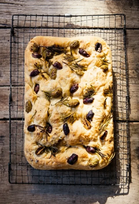 Hairy Bikers focaccia on a wire rack, golden and dimpled with olives and rosemary pressed into the top