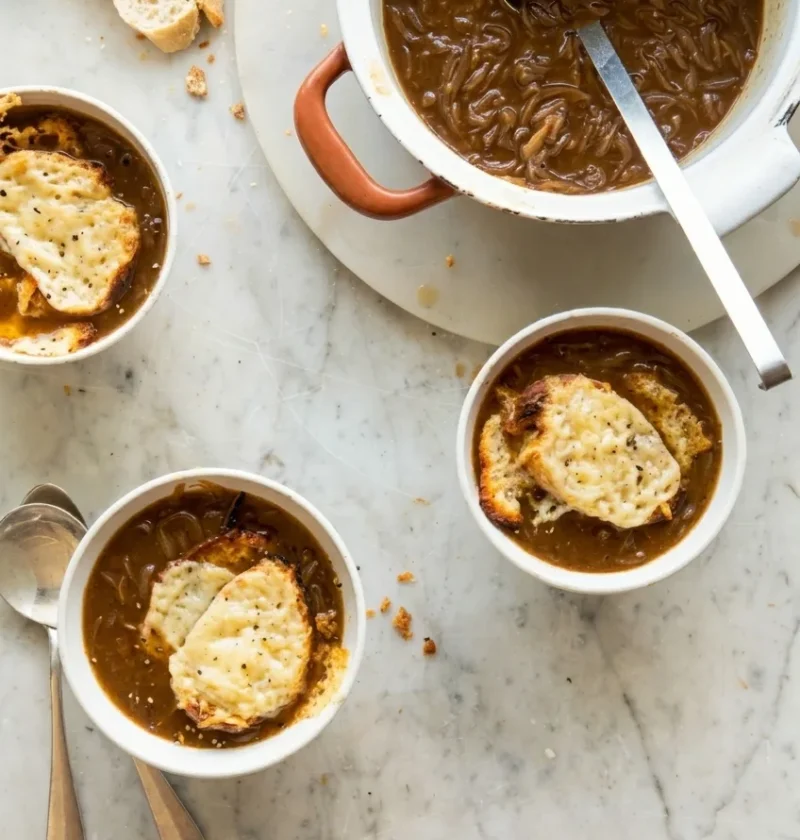 Hairy Bikers french onion soup in white bowls topped with Gruyere croutons, with a pot of caramelised onion soup alongside