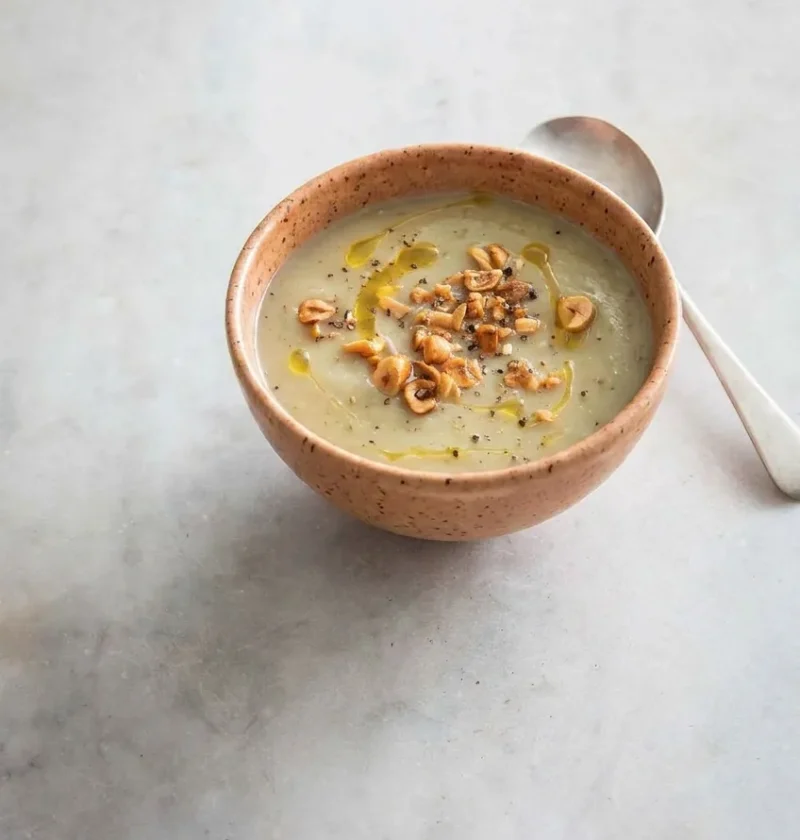 Hairy Bikers Jerusalem artichoke soup in a terracotta bowl topped with crushed toasted hazelnuts and a drizzle of oil