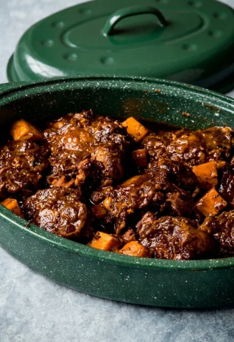 Hairy Bikers oxtail stew in a green casserole dish, oxtail on the bone in a thick dark sauce with chunks of sweet potato