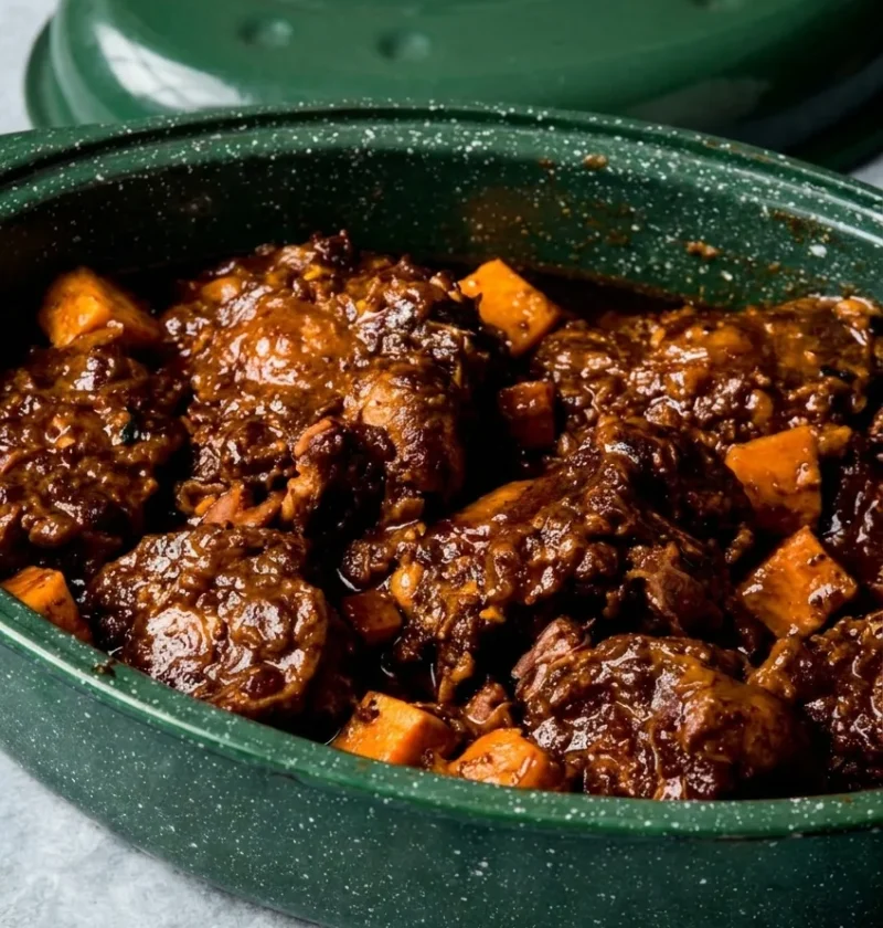 Hairy Bikers oxtail stew in a green casserole dish, oxtail on the bone in a thick dark sauce with chunks of sweet potato