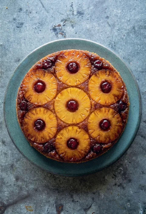 Hairy Bikers pineapple upside down cake turned out onto a plate with seven caramelised pineapple rings and a glace cherry in each hole