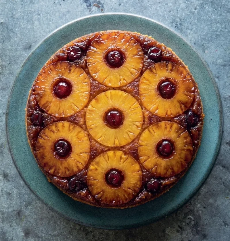 Hairy Bikers pineapple upside down cake turned out onto a plate with seven caramelised pineapple rings and a glace cherry in each hole