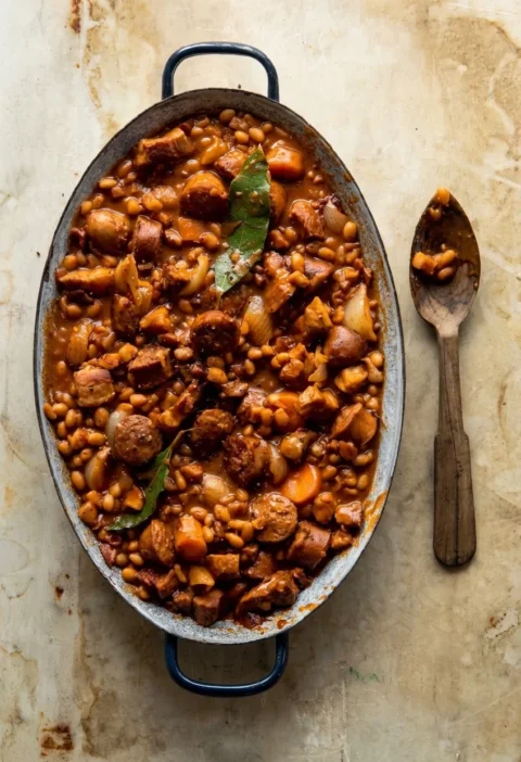 Hairy Bikers pork and bean casserole in an oval dish, haricot beans with pork belly, sausage and bay leaves in a thick sauce
