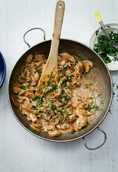 Hairy Bikers pork stroganoff in a steel pan with strips of pork, sliced mushrooms and parsley in a creamy paprika sauce