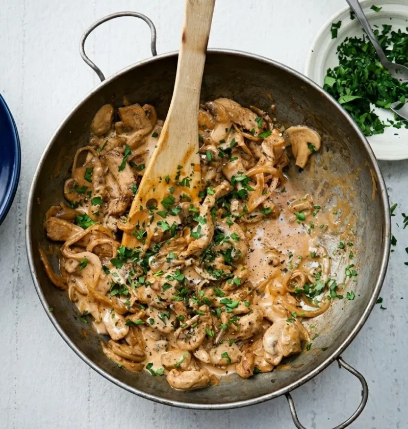 Hairy Bikers pork stroganoff in a steel pan with strips of pork, sliced mushrooms and parsley in a creamy paprika sauce