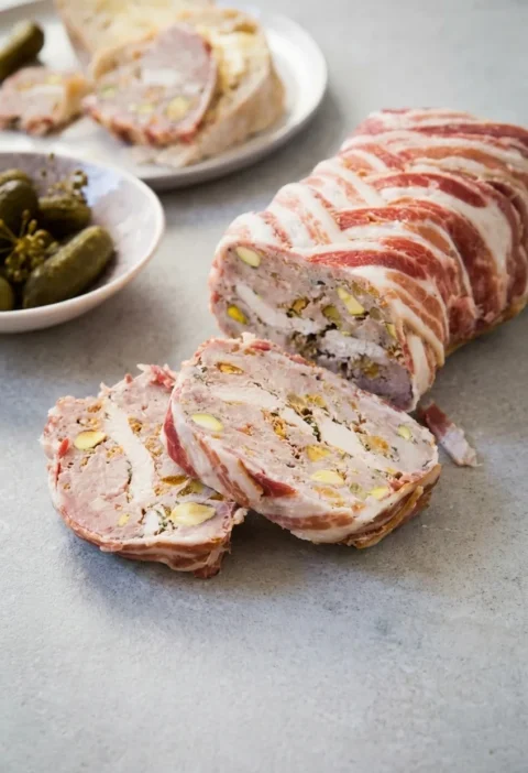 Hairy Bikers pork terrine wrapped in streaky bacon and sliced, showing pistachios, dried apricots and a band of chicken through the middle