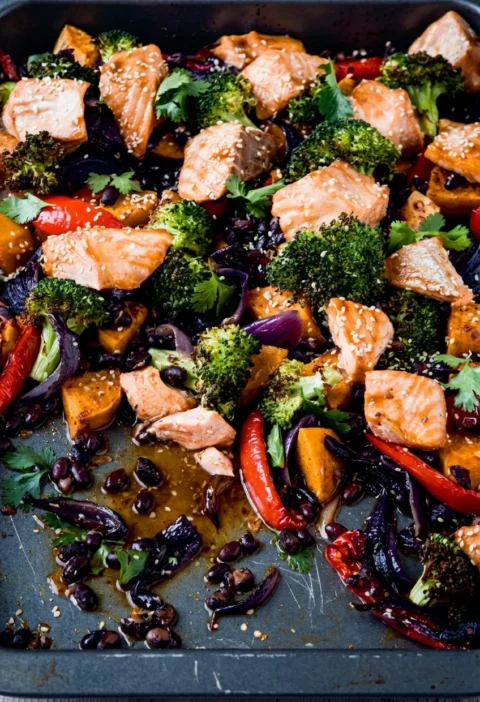 Hairy Bikers salmon tray bake in a roasting tin with pale pink salmon chunks on charred broccoli, sweet potato, red pepper and black beans