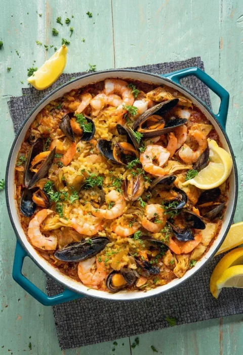 Hairy Bikers seafood paella in a shallow pan with prawns, open mussels, artichoke hearts and saffron rice