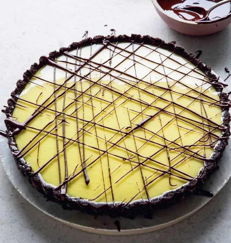 A key lime pie with a dark Oreo base and dark chocolate drizzled in lines across a green lime glaze