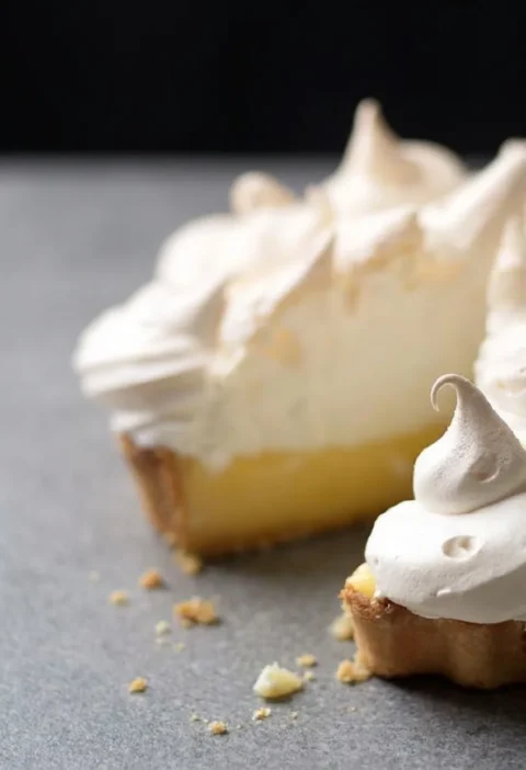 A slice cut from a lemon meringue pie showing the pastry, lemon layer and piped meringue