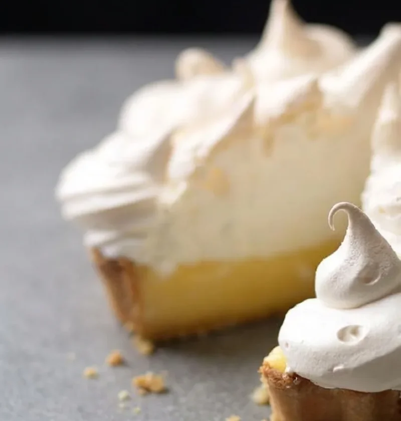 A slice cut from a lemon meringue pie showing the pastry, lemon layer and piped meringue
