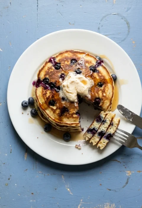 Stack of American buttermilk pancakes with blueberries, whipped maple butter and maple syrup, a wedge cut out