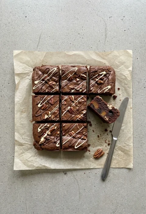 Sweet potato brownies cut into squares with dark and white chocolate drizzle and pecans, one on its side showing caramelised sweet potato