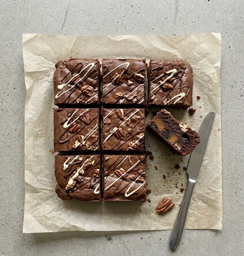Sweet potato brownies cut into squares with dark and white chocolate drizzle and pecans, one on its side showing caramelised sweet potato