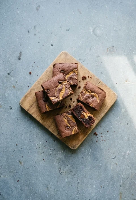 Vegan brownies with swirls of peanut butter and chocolate chips on a wooden board, one broken open to show the soft inside