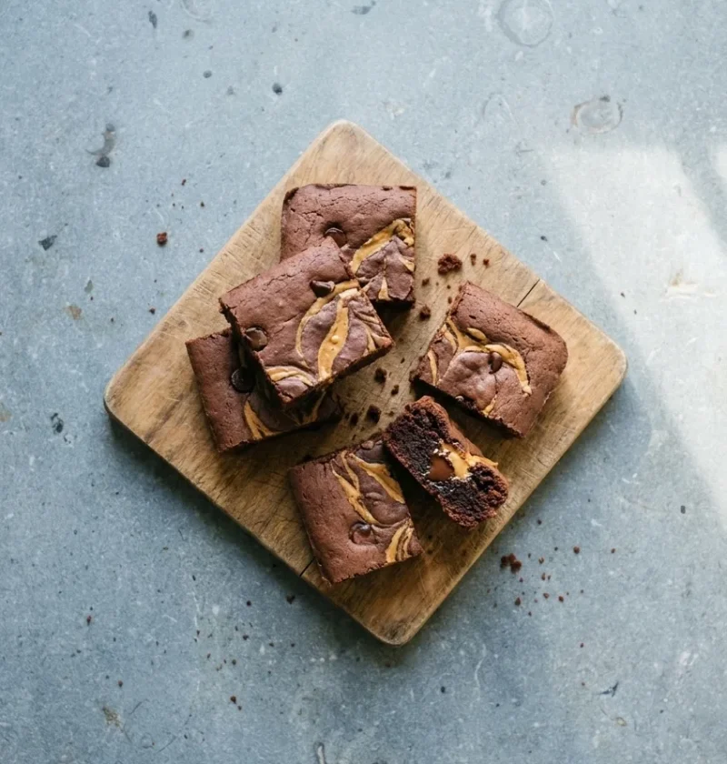 Vegan brownies with swirls of peanut butter and chocolate chips on a wooden board, one broken open to show the soft inside